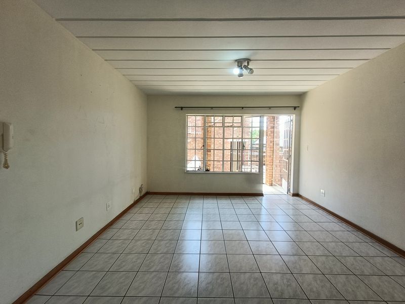 An empty, open-plan living area featuring tiled flooring, ceiling panels, and direct access to an outdoor space through a security gate.