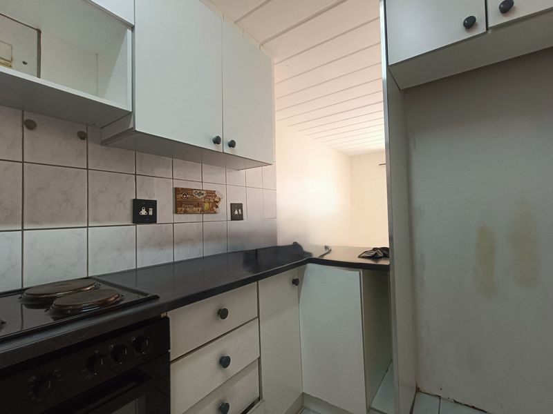 A compact kitchen featuring built-in cabinetry, a dark laminate countertop, an electric hob and oven, and a tiled backsplash.