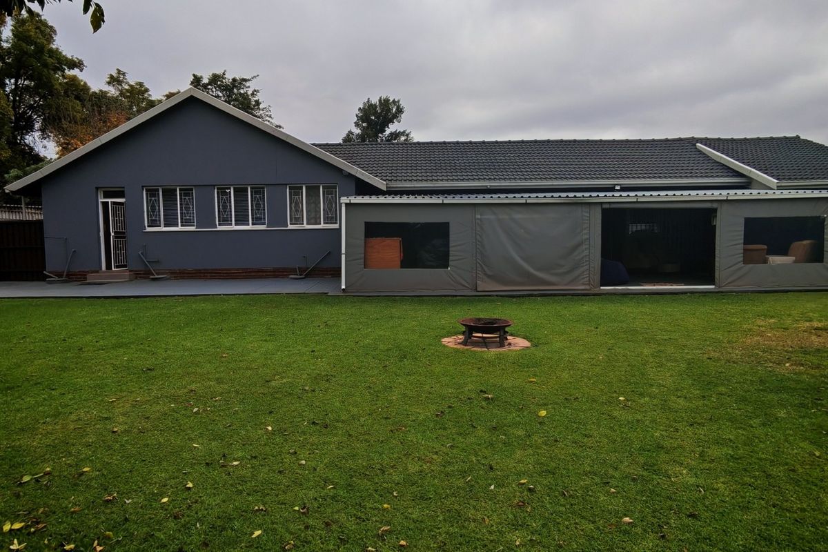 Rear view of the property featuring a spacious lawn, a covered patio area with protective canvas enclosures, and a well-maintained tiled roof.