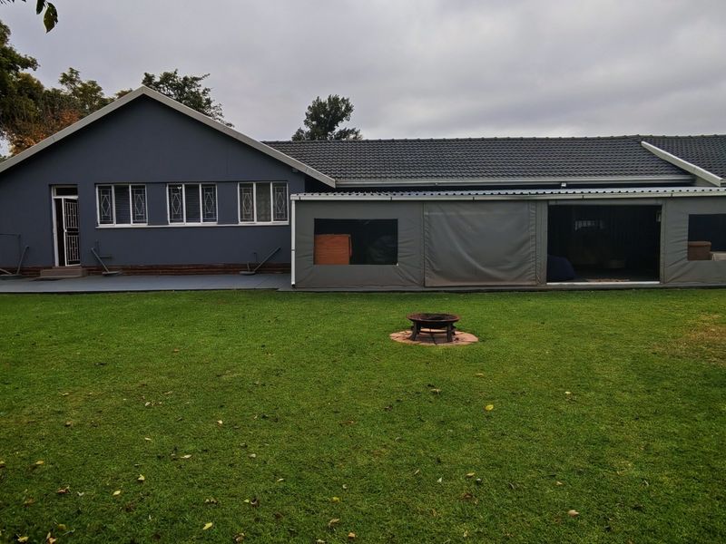 Rear view of the property featuring a spacious lawn, a covered patio area with protective canvas enclosures, and a well-maintained tiled roof.