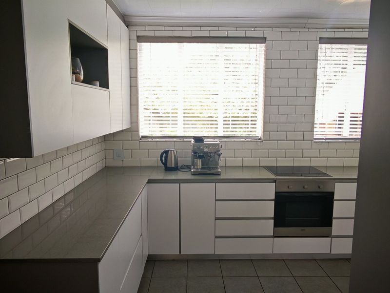 Modern kitchen featuring white handleless cabinetry, grey quartz countertops, subway tile backsplash, and integrated stainless steel oven and cooktop.