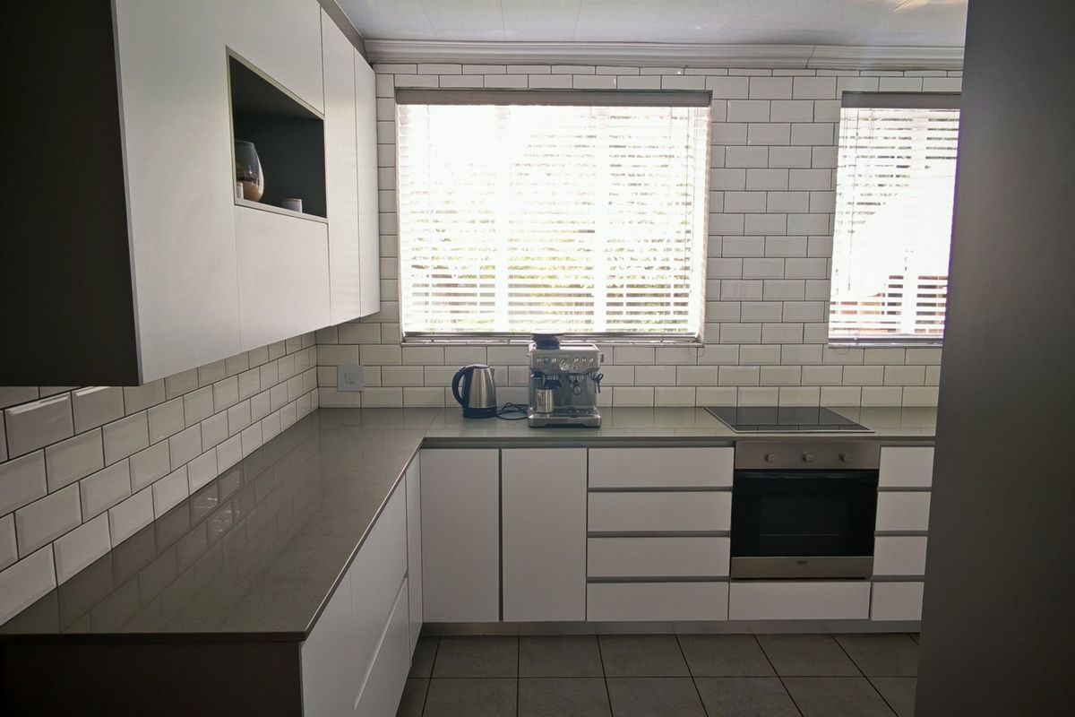 Modern kitchen featuring white handleless cabinetry, grey quartz countertops, subway tile backsplash, and integrated stainless steel oven and cooktop.