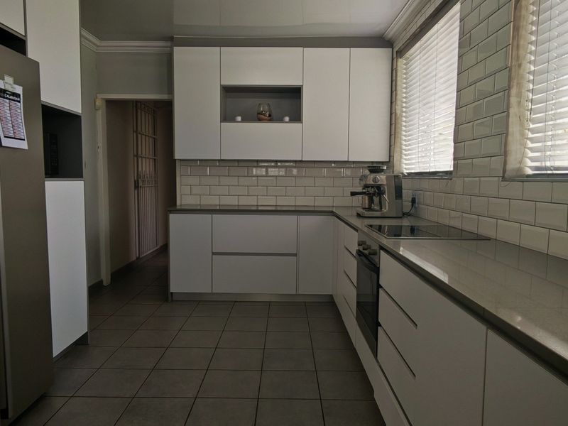 Modern kitchen featuring white cabinetry, subway tile backsplash, stone countertops, and integrated appliances with neutral ceramic floor tiles.