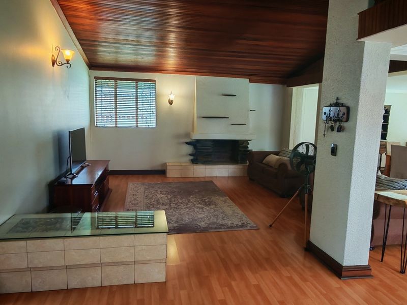 Spacious open-plan living area featuring a striking timber-clad vaulted ceiling, a built-in fireplace, and warm laminate flooring throughout.