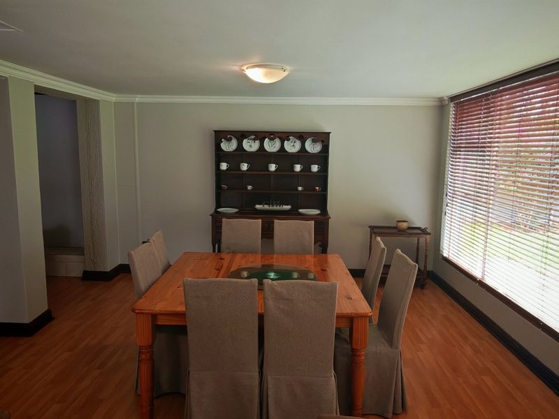 A dining room featuring laminate flooring, crown molding, and large windows fitted with venetian blinds, providing a bright and functional space.