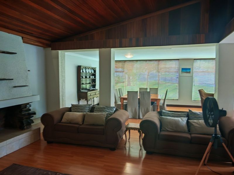 Spacious open-plan living and dining area featuring a prominent stone fireplace, warm timber raked ceilings, and laminate flooring with natural light.