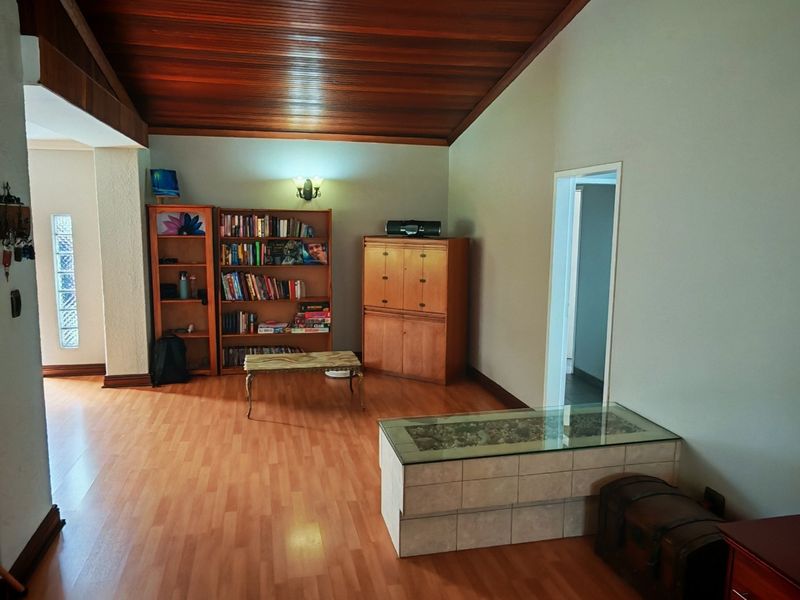 Spacious living area featuring a high vaulted timber ceiling, laminate flooring, and a unique glass block accent wall, offering a warm and inviting atmosphere.