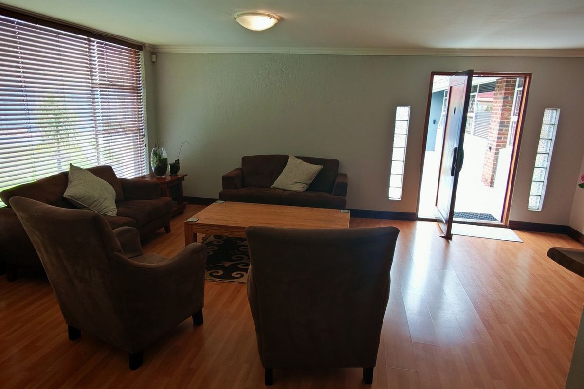 A living room featuring laminate flooring, large windows with venetian blinds, and glass block sidelights flanking the main entrance door.