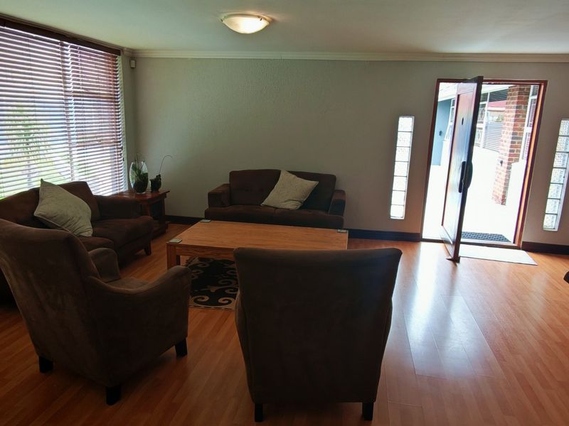 A living room featuring laminate flooring, large windows with venetian blinds, and glass block sidelights flanking the main entrance door.