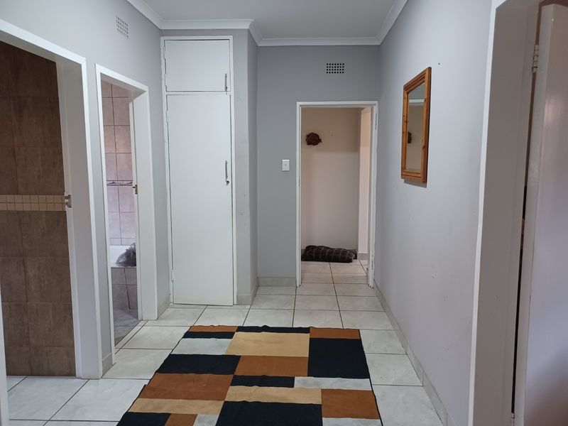A clean and functional hallway featuring neutral grey walls, tiled flooring, and a built-in storage cupboard, providing access to adjacent rooms.