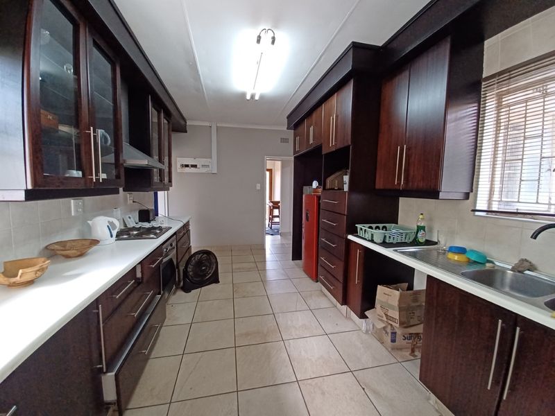 A functional galley-style kitchen featuring dark wood cabinetry, a gas hob, built-in oven, and tiled flooring with ample counter space.