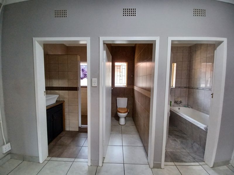 A functional bathroom layout featuring separate compartments for the vanity, toilet, and bathtub with tiled finishes throughout.