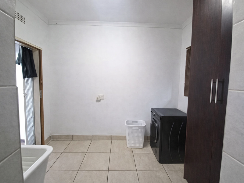 A functional laundry room featuring tiled flooring, built-in storage cabinetry, and direct access to the exterior via a security gate.
