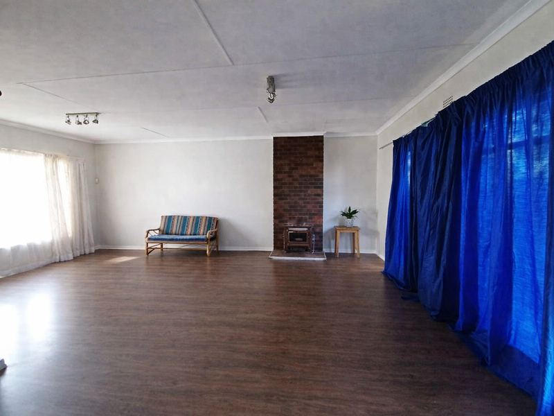 Spacious living room featuring wood-look laminate flooring, a central brick fireplace, and ample natural light from large windows.