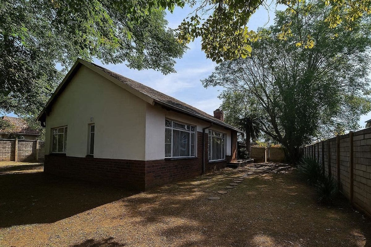 Rear view of a single-story brick house featuring a tiled roof, steel-framed windows, and a large private garden enclosed by a brick boundary wall.