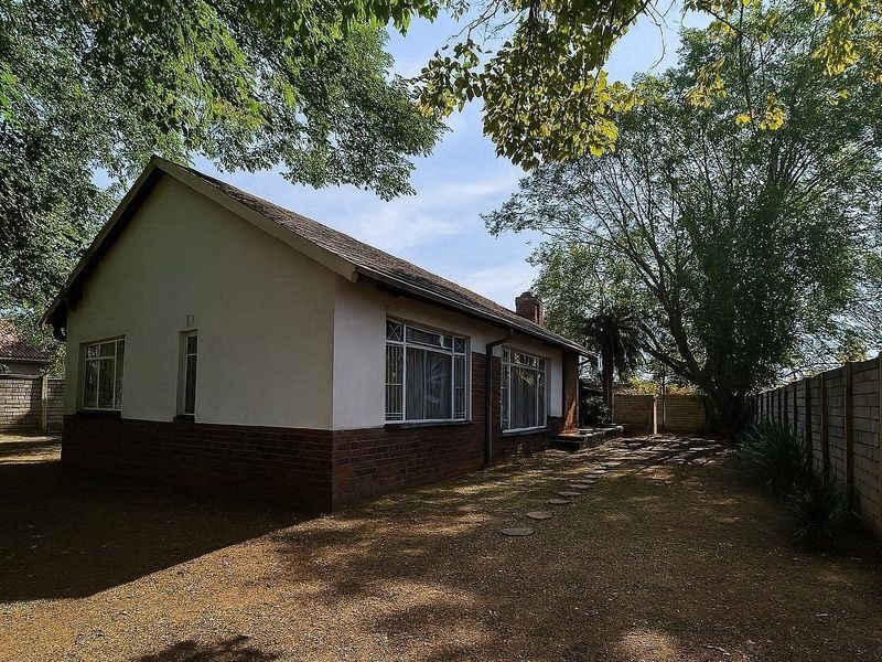 Rear view of a single-story brick house featuring a tiled roof, steel-framed windows, and a large private garden enclosed by a brick boundary wall.