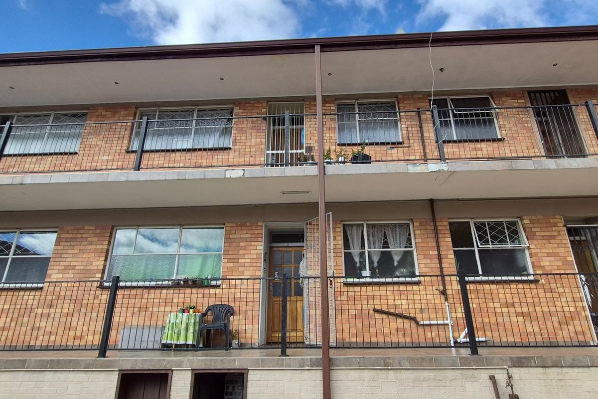 Rear elevation of a multi-story flat building featuring brick facade, metal balustrades, and tiled balcony access for upper and lower units.