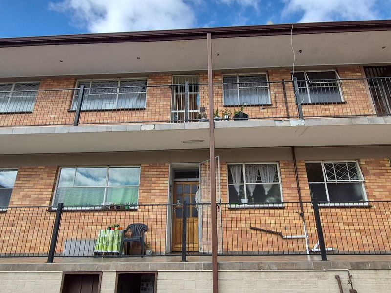 Rear elevation of a multi-story flat building featuring brick facade, metal balustrades, and tiled balcony access for upper and lower units.