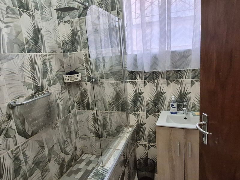 A compact bathroom featuring patterned wall tiles, a vanity basin, and a shower area with a glass screen.