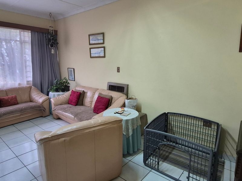 A living room featuring tiled flooring, a large window with curtains, and a wall-mounted heater.