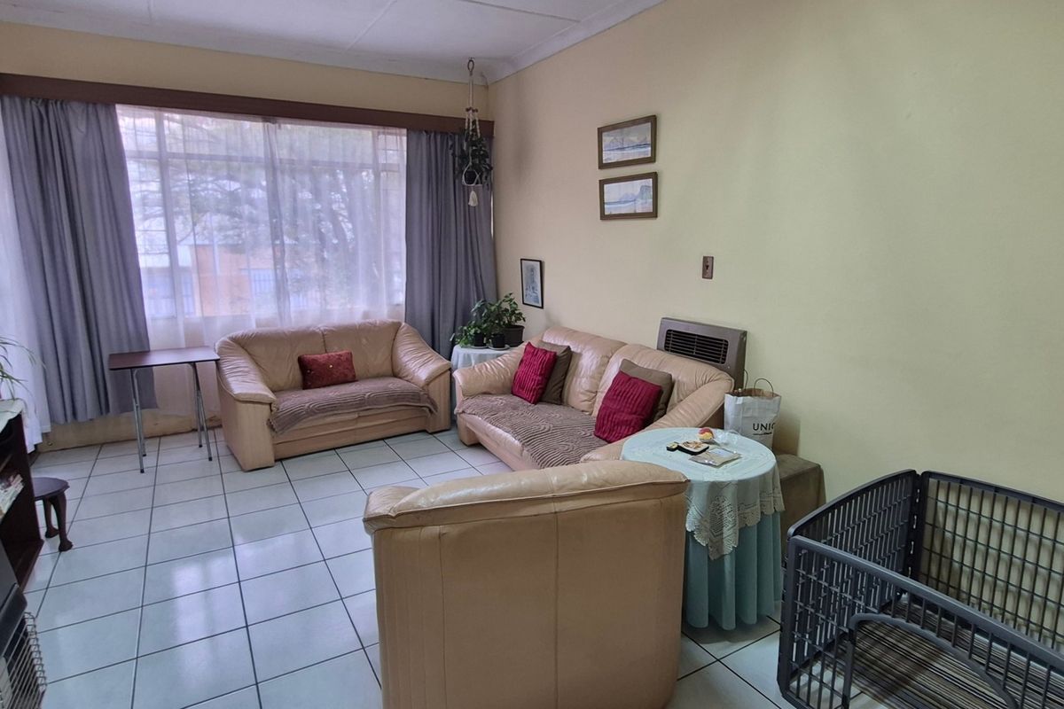 A living room featuring tiled flooring, a large window providing natural light, and a built-in wall heater.