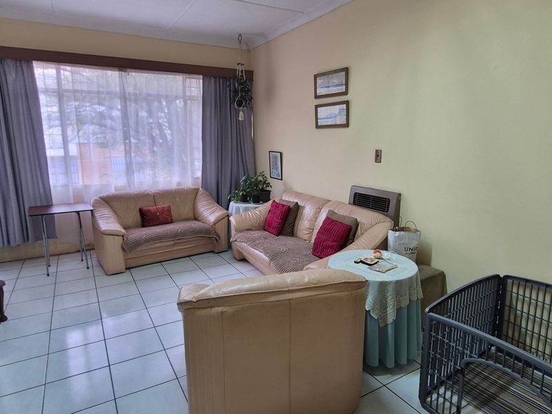 A living room featuring tiled flooring, a large window providing natural light, and a built-in wall heater.