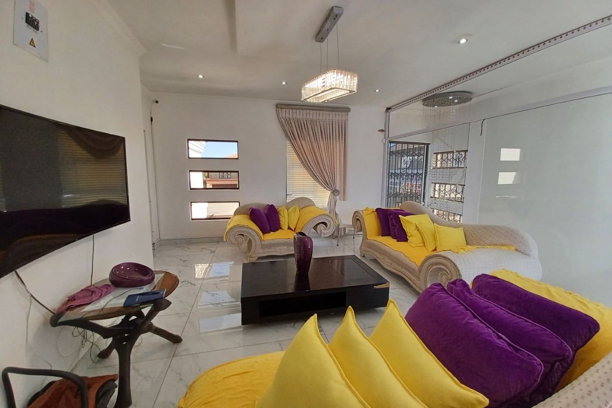 Spacious living room featuring polished marble-look flooring, recessed ceiling lighting, a modern crystal chandelier, and large sliding glass doors providing natural light.