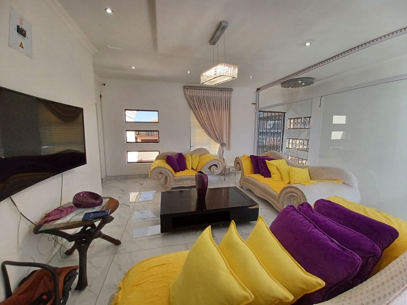 Spacious living room featuring polished marble-look flooring, recessed ceiling lighting, a modern crystal chandelier, and large sliding glass doors providing natural light.