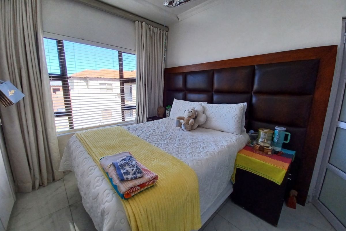 A well-maintained bedroom featuring a large built-in headboard, tiled flooring, and natural light through a window fitted with venetian blinds and curtains.