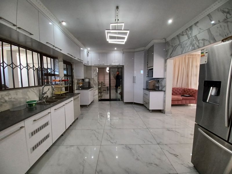 Modern kitchen featuring high-gloss cabinetry, marble-look floor tiles, double sink, and contemporary pendant lighting, with an open flow to the adjacent living area.
