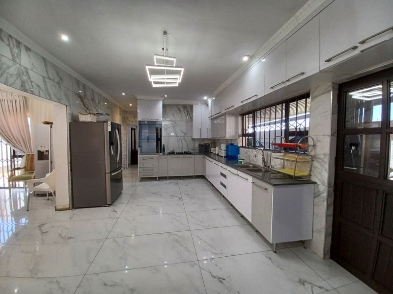 Modern kitchen featuring high-gloss cabinetry, marble-look wall and floor tiles, built-in oven, gas hob, and contemporary lighting fixtures.