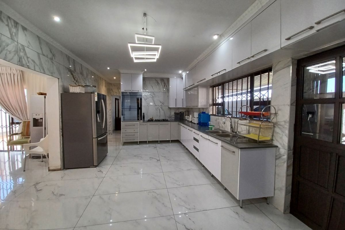 Modern kitchen featuring high-gloss cabinetry, marble-look wall and floor tiles, built-in oven, gas hob, and contemporary lighting fixtures.