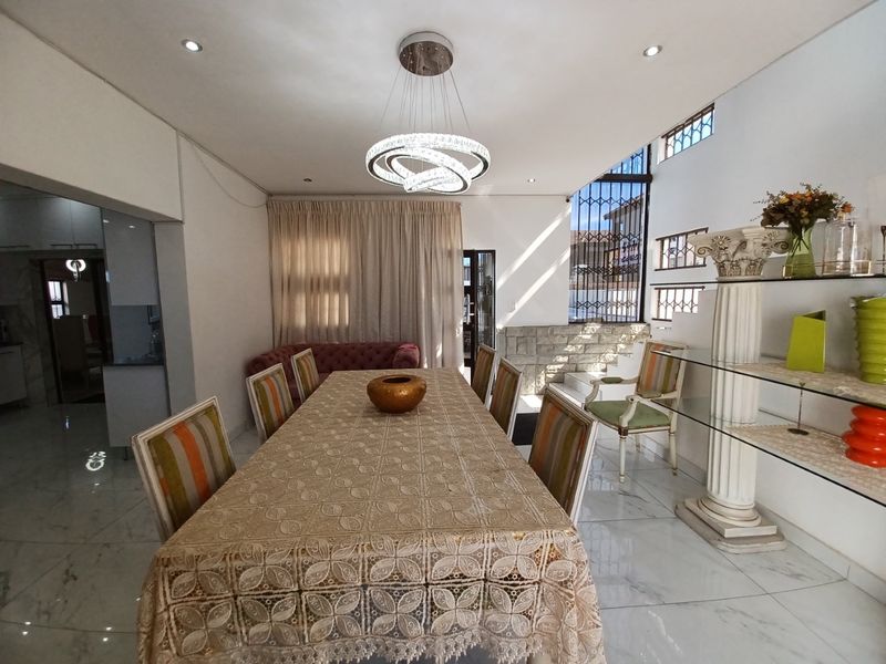 Spacious dining room featuring polished marble-look flooring, a modern statement chandelier, and a decorative stone feature wall with natural light.
