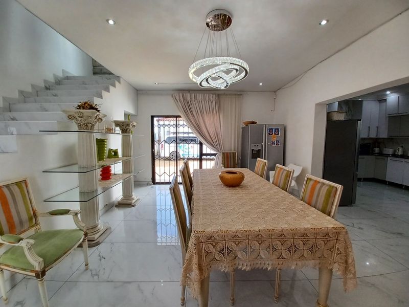 Spacious open-plan dining area featuring polished marble-look flooring, a modern crystal chandelier, and an integrated staircase, flowing seamlessly into the adjacent kitchen.