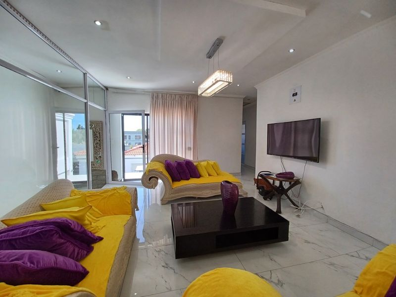 A bright living room featuring marble-look floor tiles, recessed downlighting, a modern pendant fixture, and a sliding glass door leading to the exterior.