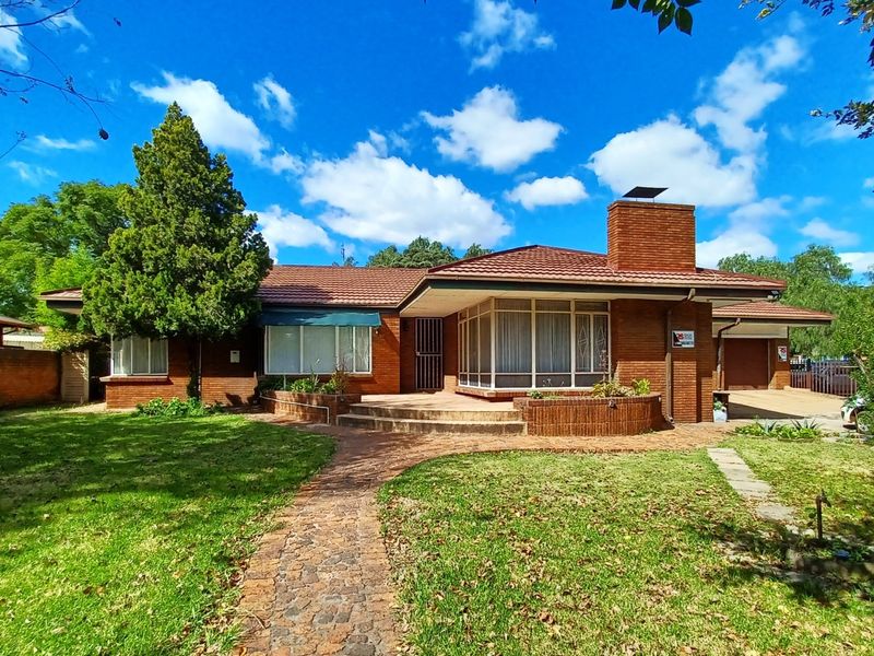A classic single-story brick house featuring a tiled roof, prominent brick chimney, paved front walkway, and an attached garage set within a landscaped garden.