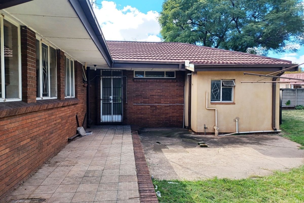 Rear exterior view of the house featuring a brick facade, tiled roof, paved patio area, and a concrete apron leading to the garden.