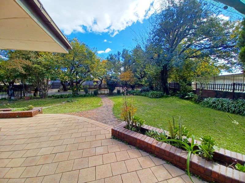 A spacious paved patio area overlooking a well-maintained garden with a brick planter box and a cobblestone path leading through the lawn.