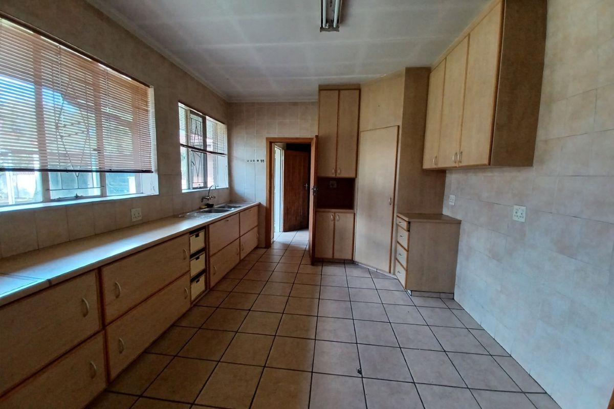 A spacious, empty kitchen featuring extensive built-in cabinetry, tiled flooring, and wall tiling, offering a functional layout ready for modernization.