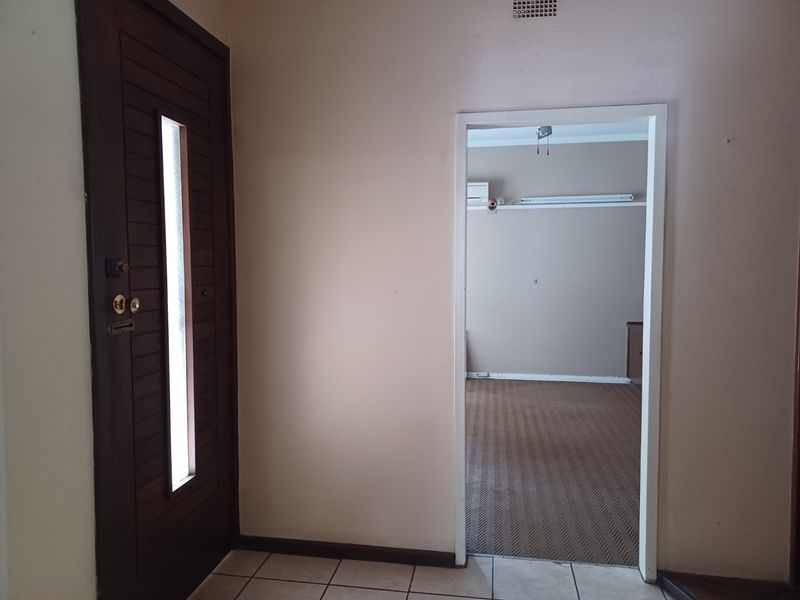 Entrance foyer featuring a timber front door and tiled flooring, leading into an empty carpeted room with an installed air conditioning unit.