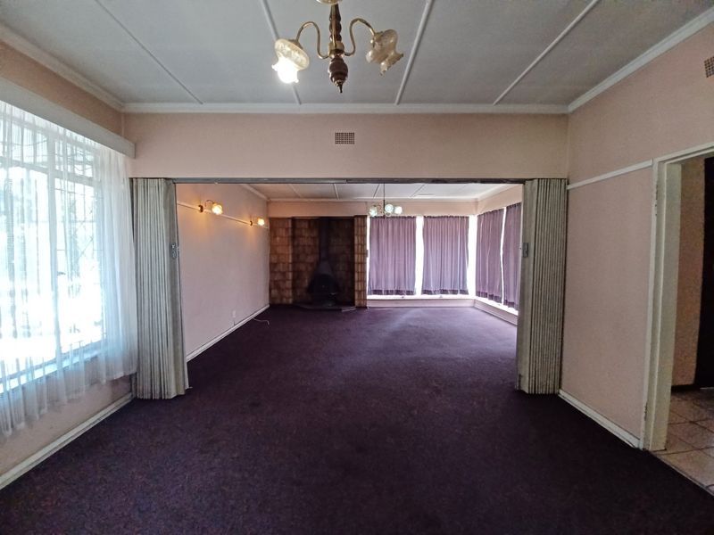 Spacious living area featuring a central fireplace, folding room dividers, and classic ceiling lighting, offering a versatile layout ready for modernization.