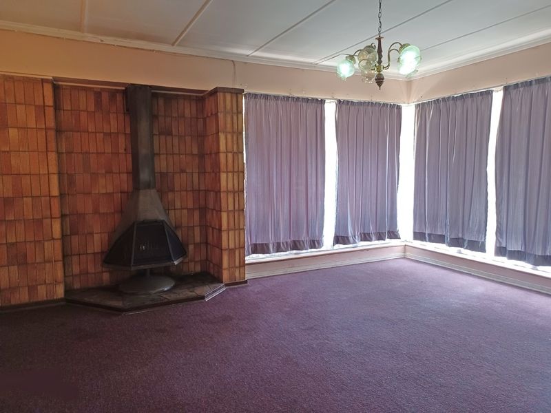 Spacious living room featuring a unique freestanding fireplace with a tiled surround, large windows, and original ceiling details, ready for modernization.