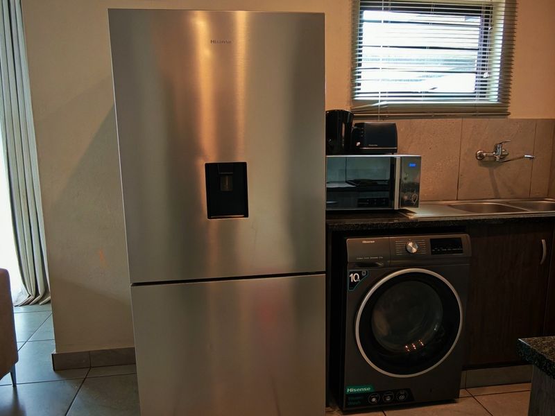 A functional scullery area featuring a stainless steel sink, granite countertops, built-in cabinetry, and space for laundry appliances.