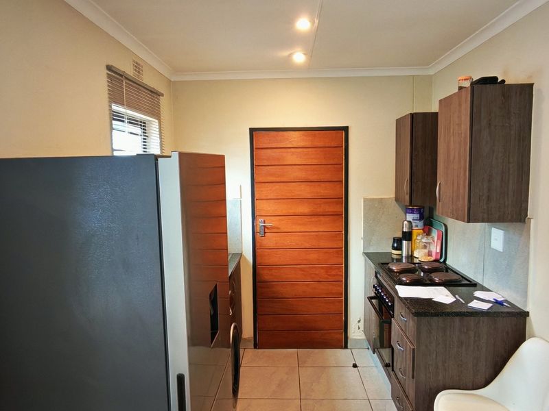 Compact kitchen featuring dark wood cabinetry, built-in hob and oven, tiled flooring, and a wooden door leading to the exterior.