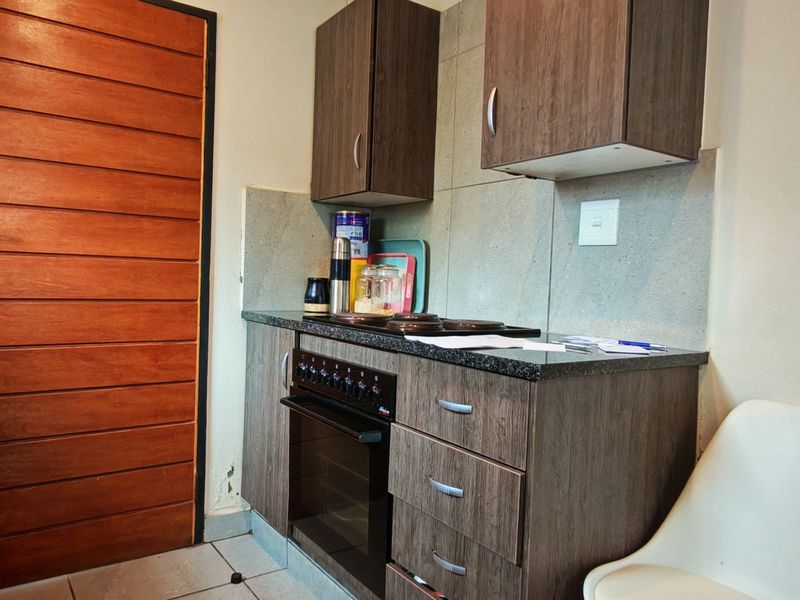 Compact kitchen featuring dark wood-look cabinetry, granite countertops, built-in oven and hob, and tiled flooring.