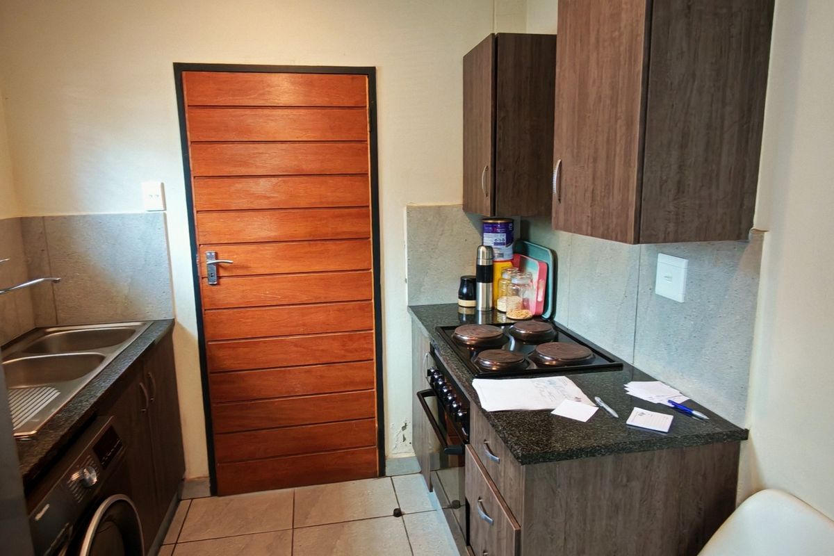 Compact kitchen featuring dark wood cabinetry, granite countertops, integrated electric hob and oven, and tiled flooring with a wooden door entrance.
