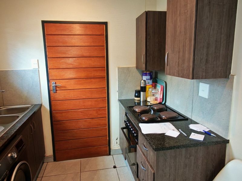 Compact kitchen featuring dark wood cabinetry, granite countertops, integrated electric hob and oven, and tiled flooring with a wooden door entrance.