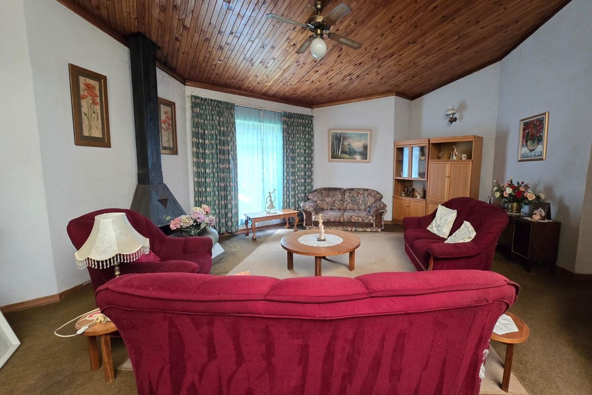 Spacious living room featuring a vaulted wood-paneled ceiling, a central ceiling fan, and a prominent freestanding metal fireplace.