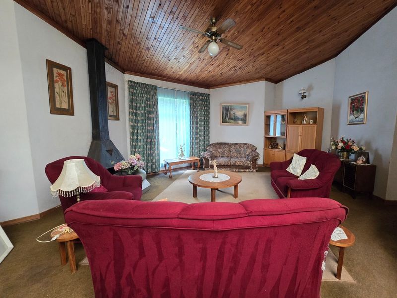Spacious living room featuring a vaulted wood-paneled ceiling, a central ceiling fan, and a prominent freestanding metal fireplace.
