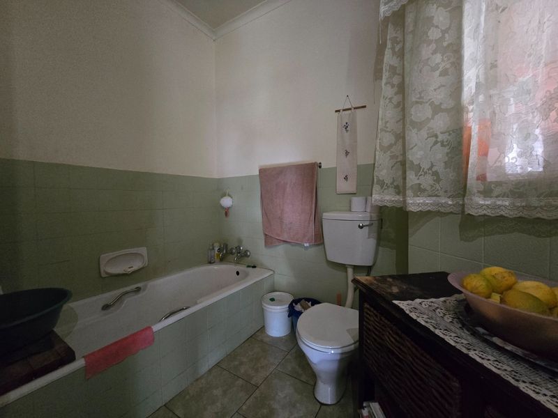 A dated bathroom featuring a built-in bathtub, toilet, and green wall tiling, offering potential for a modern renovation.
